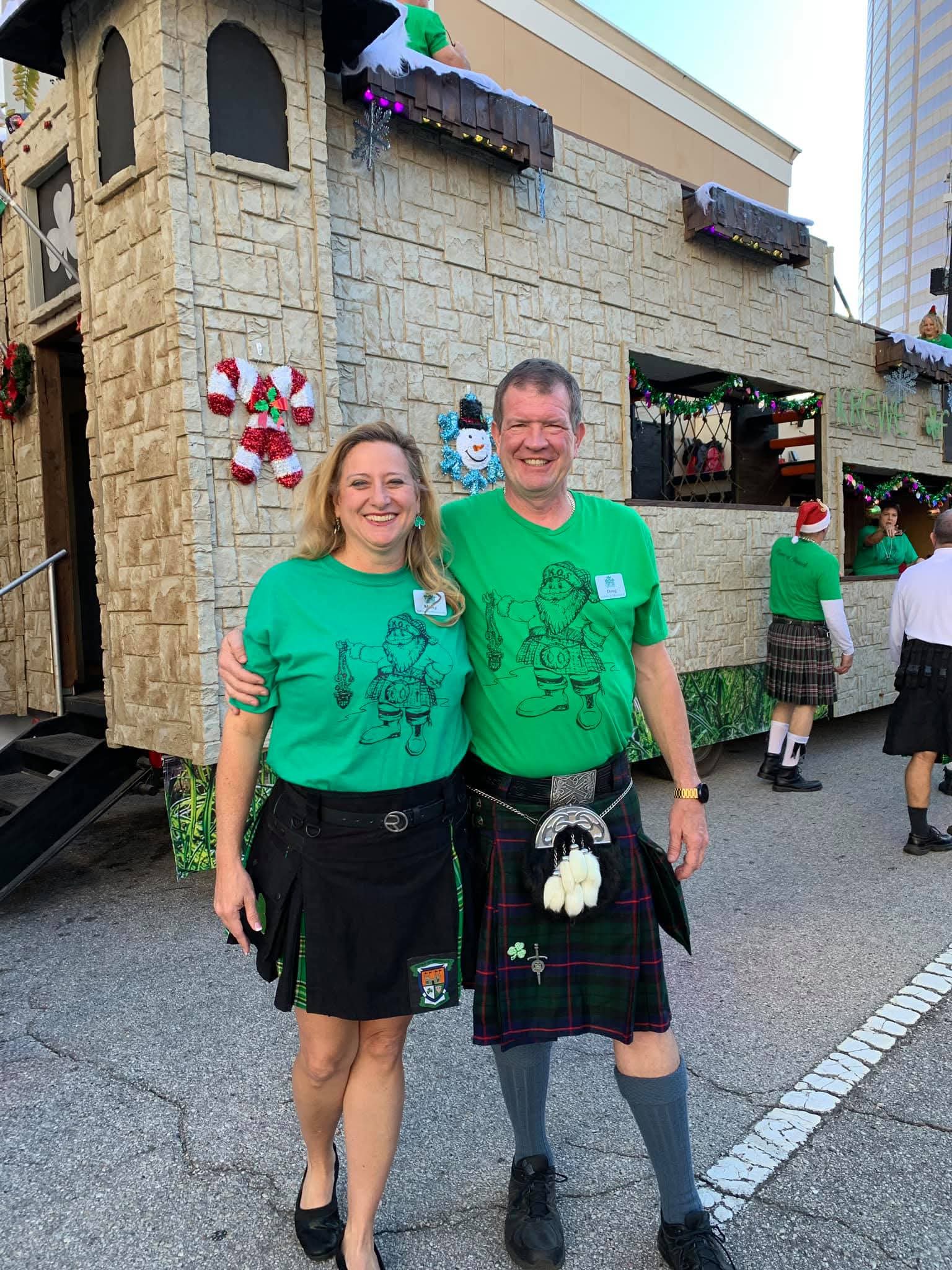 Two Krewe of Shamrock members in matching green shirts and kilts in front of the castle float